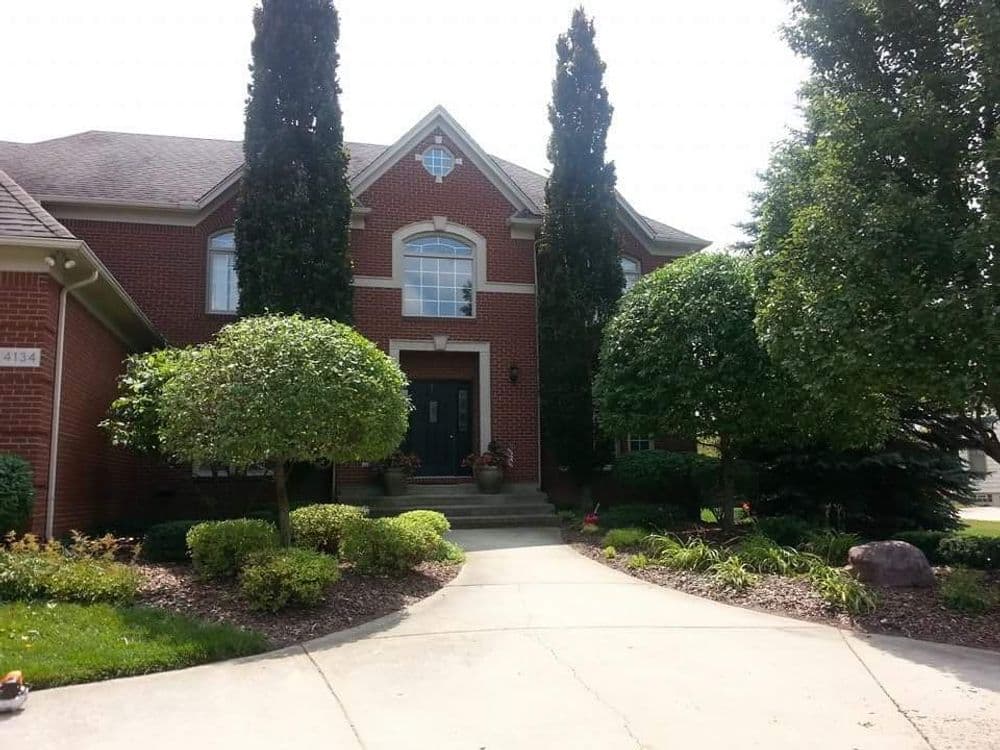 Elegant red brick home with tall trees and manicured shrubs on a sunny day.