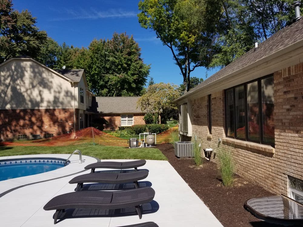 Backyard pool area with loungers, landscaping, and homes under a clear blue sky.