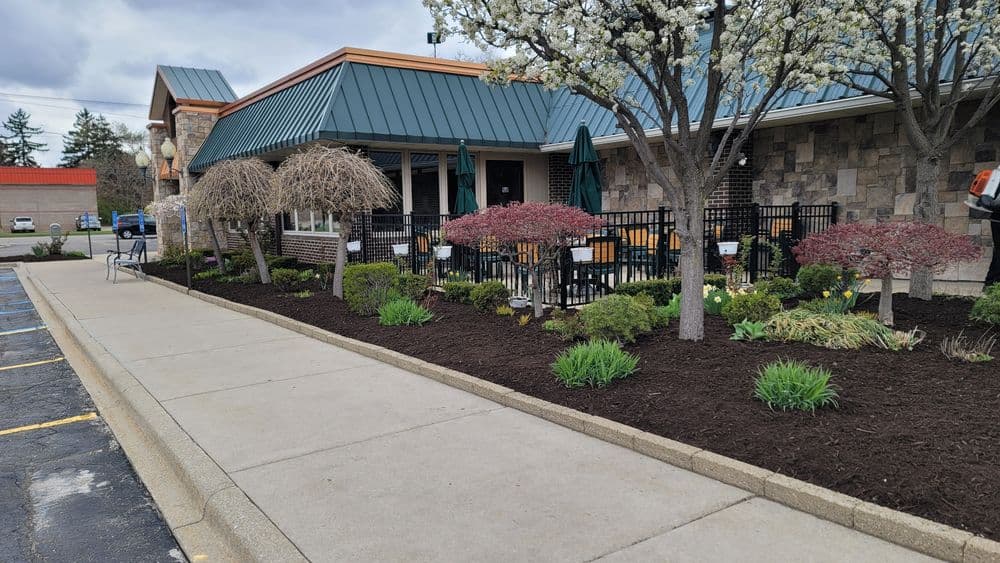 Restaurant exterior featuring landscaped garden, patio seating, and flowering trees.