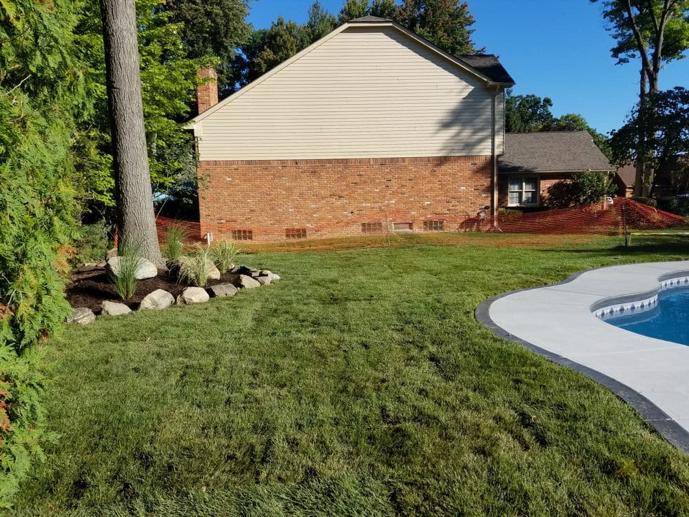 Backyard landscape featuring a manicured lawn, pool, and home with brick and siding exterior.