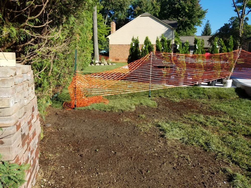 Construction site with safety fencing, freshly turned soil, and green grass in the background.
