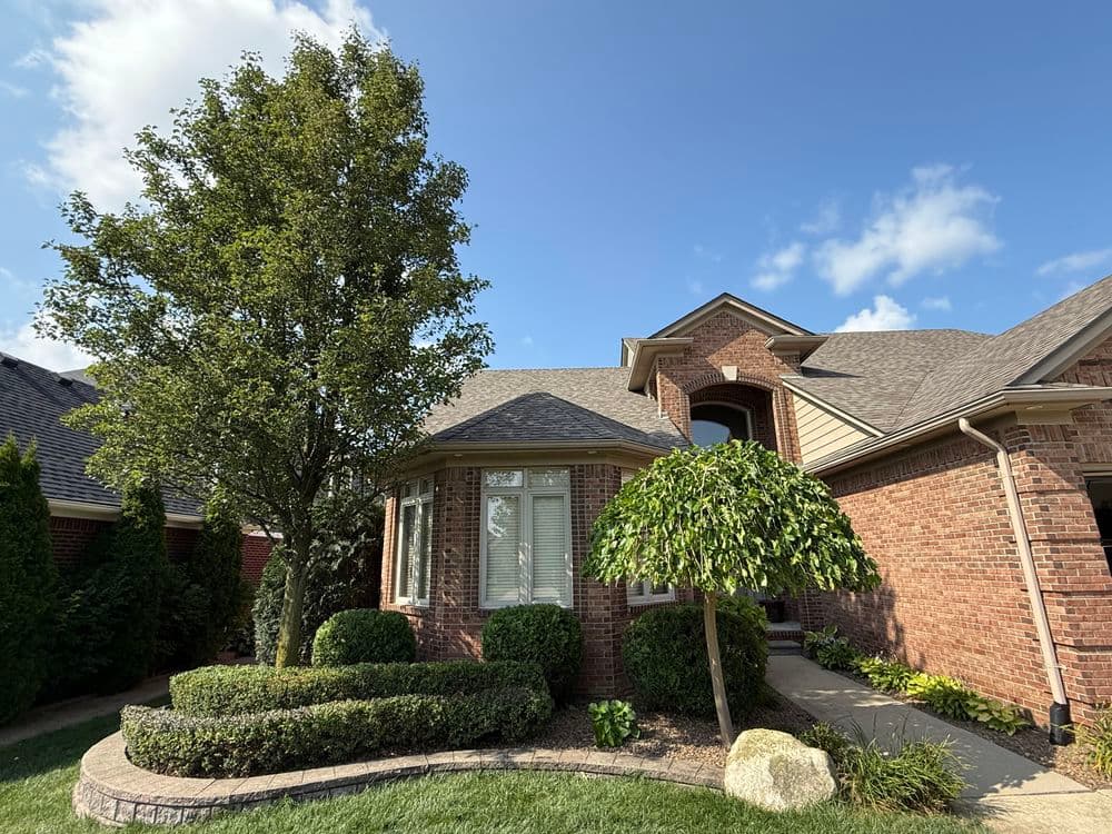 Brick house with well-maintained landscaping, including trees and shrubs, under a blue sky.