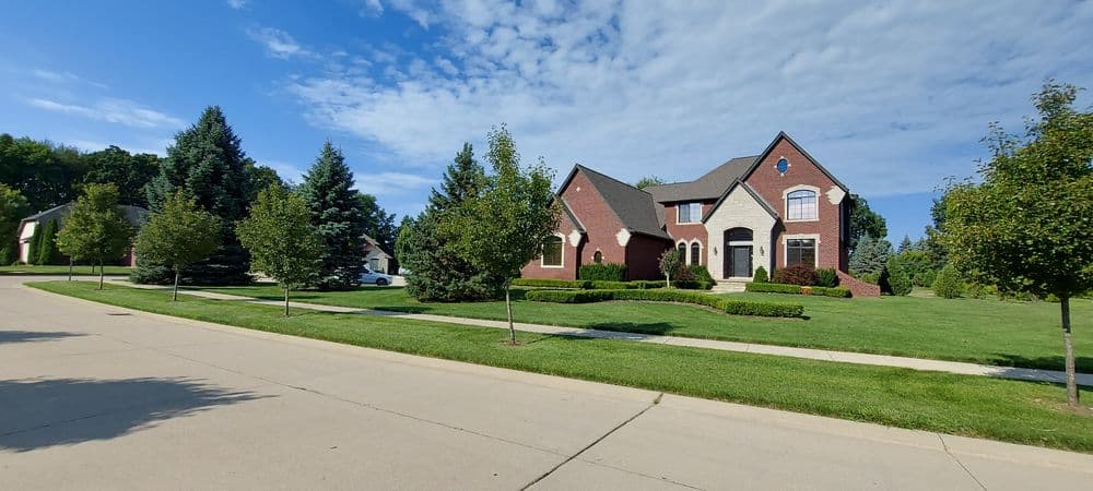 Brick house with landscaped yard and trees on a sunny day in a suburban neighborhood.