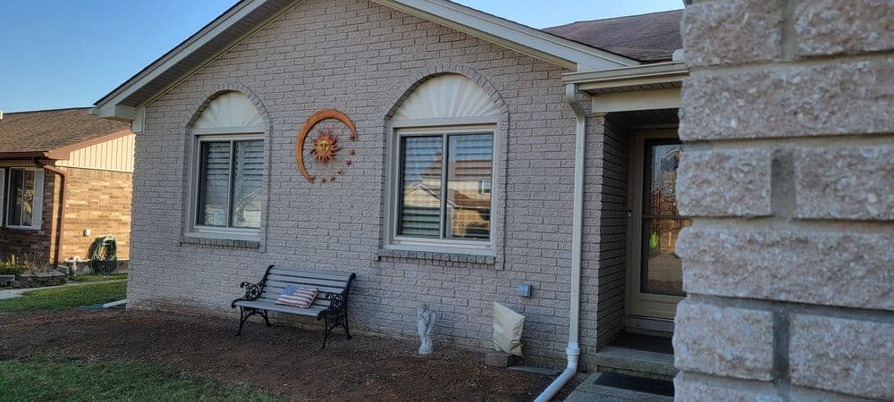 Brick home exterior with sun decor, bench, and landscaping in a suburban neighborhood.