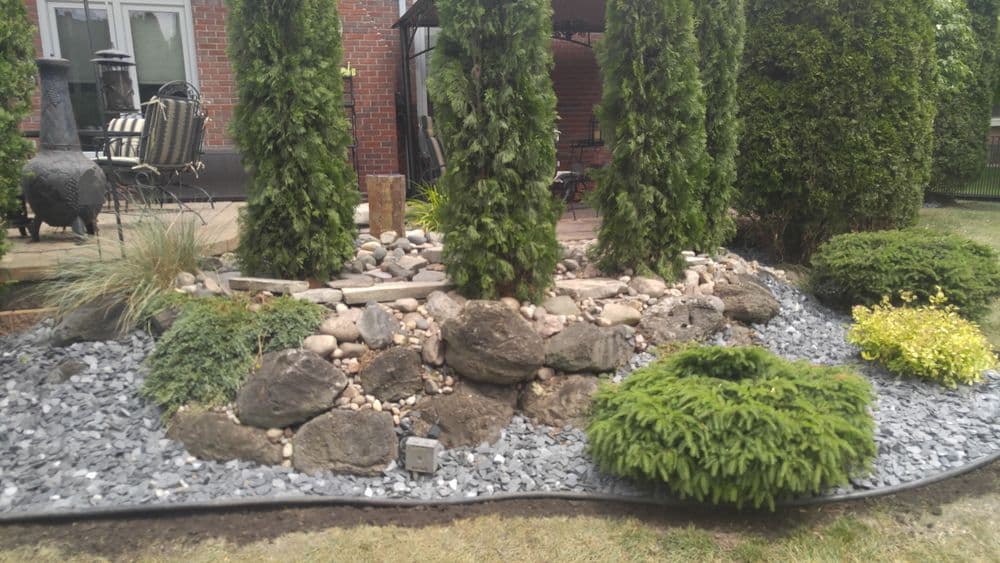 Landscape design featuring decorative stones, shrubs, and trees in a serene garden setting.