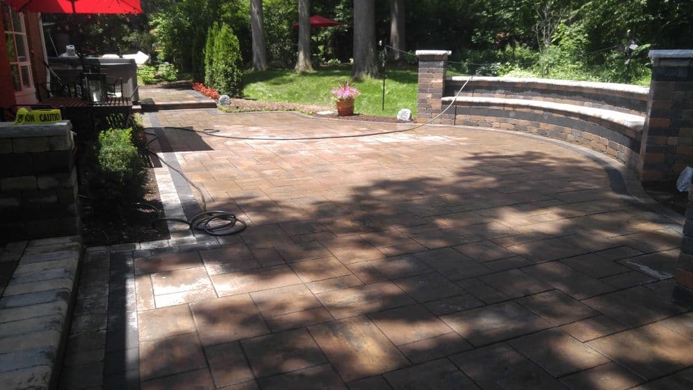 Paved outdoor patio with stone seating, surrounded by trees and garden features.