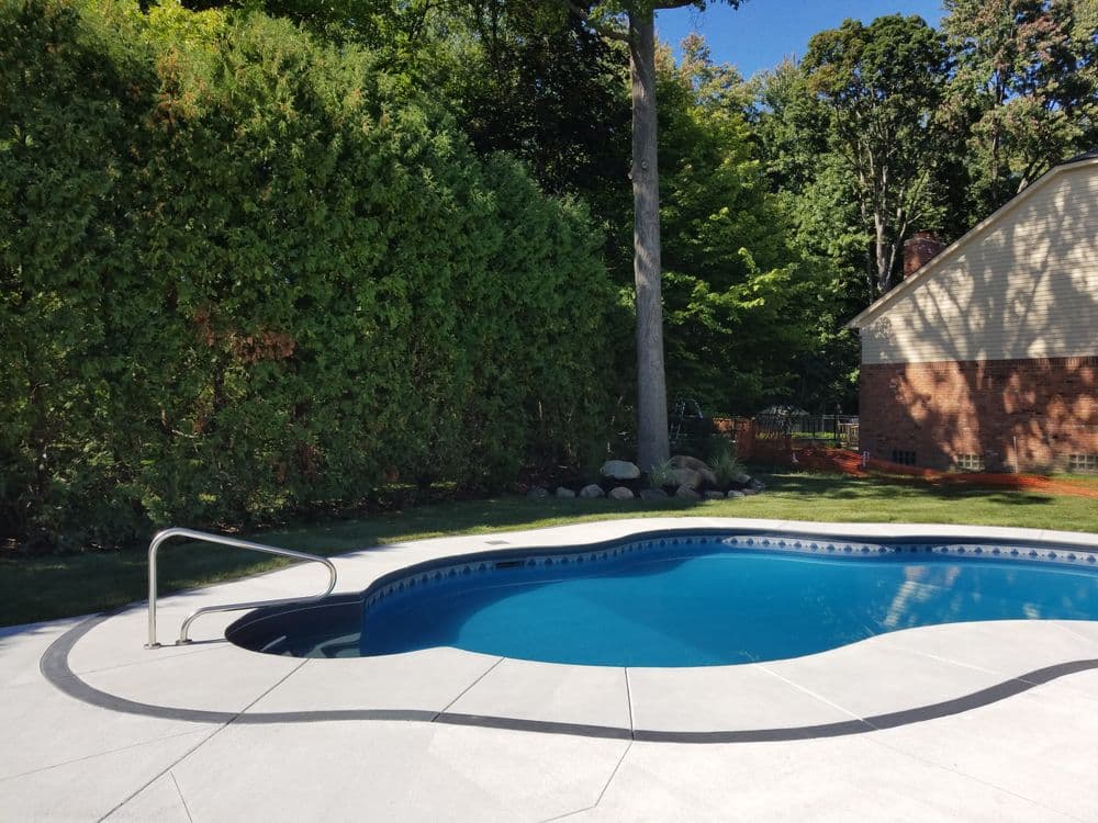 In-ground swimming pool surrounded by lush greenery and a modern home. Bright sunny day.