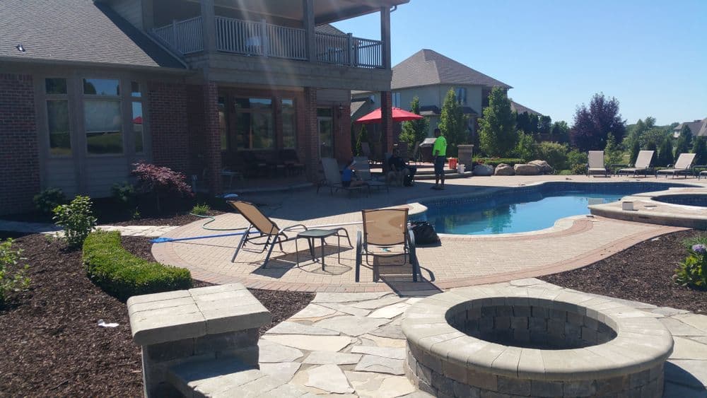 Backyard pool area with lounge chairs, patio, and landscaped garden. Sunny day with outdoor seating.