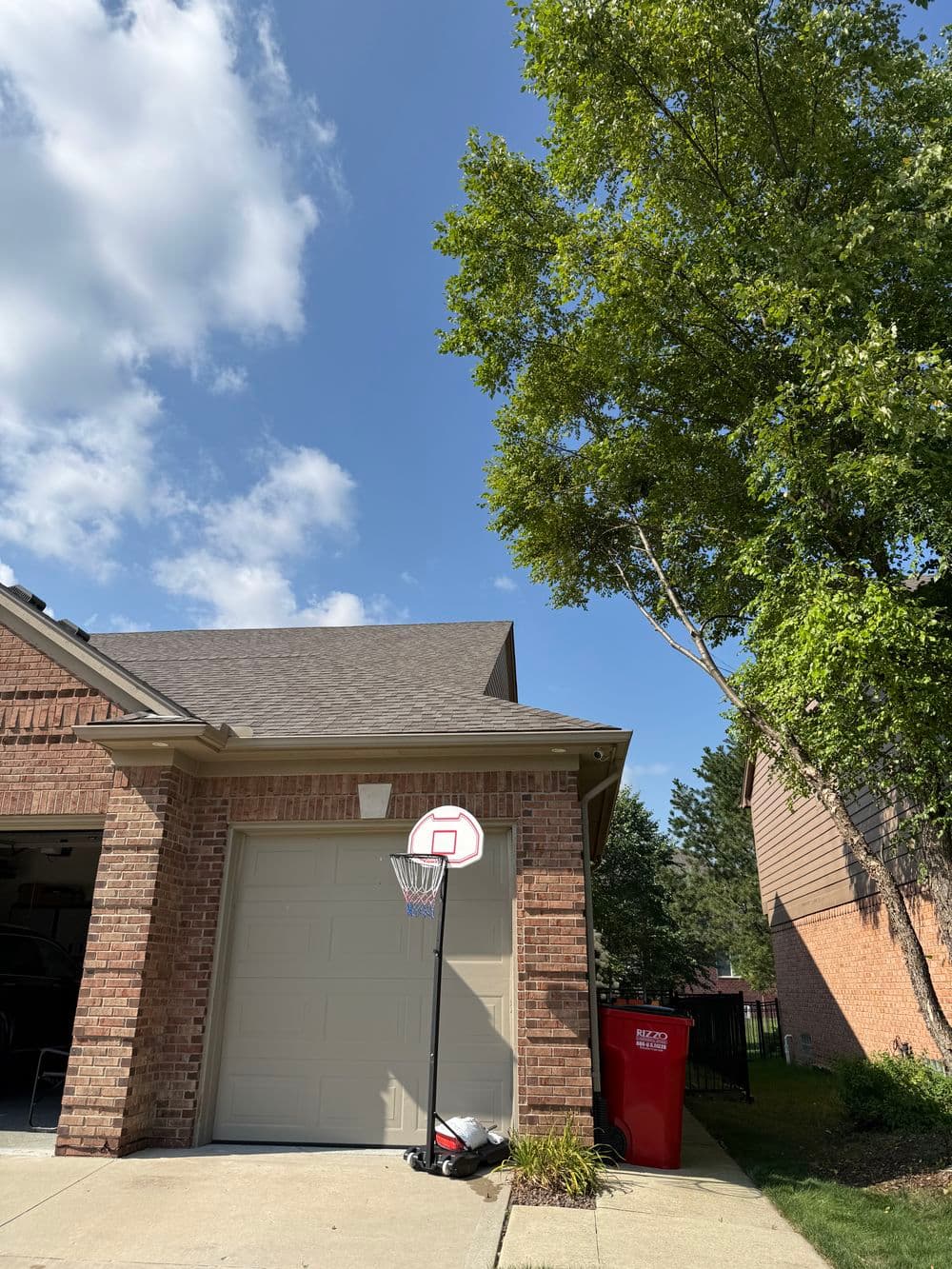 Basketball hoop beside garage in residential neighborhood with blue sky and trees.