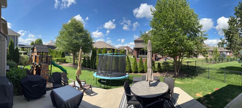 View of a backyard with a trampoline, patio furniture, and playground equipment under a clear sky.