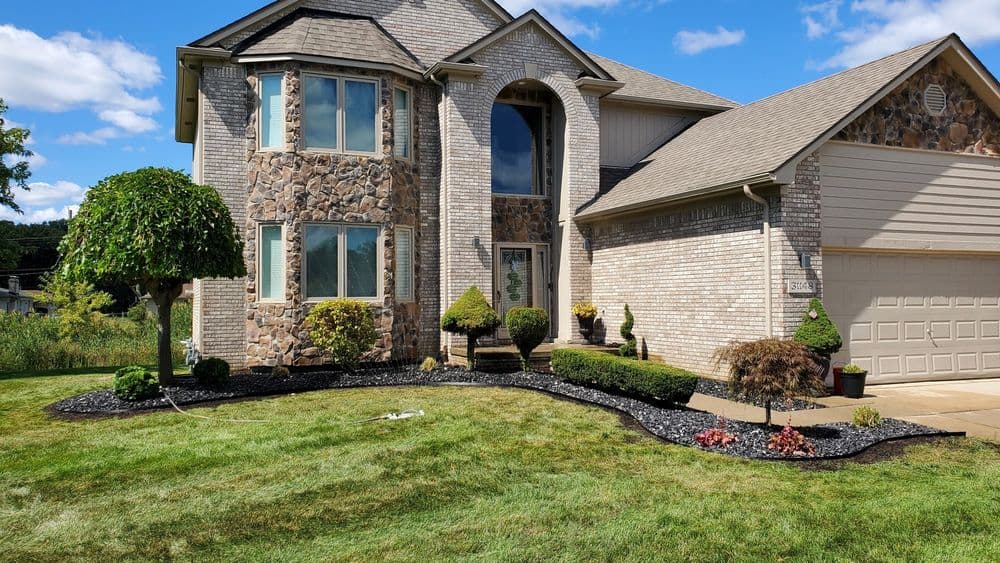 Modern stone-faced home with landscaped yard, manicured shrubs, and clear blue sky.